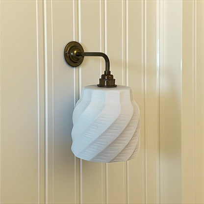 minimalist wall sconce with white glass shade and brass fixture on a beige paneled wall.
