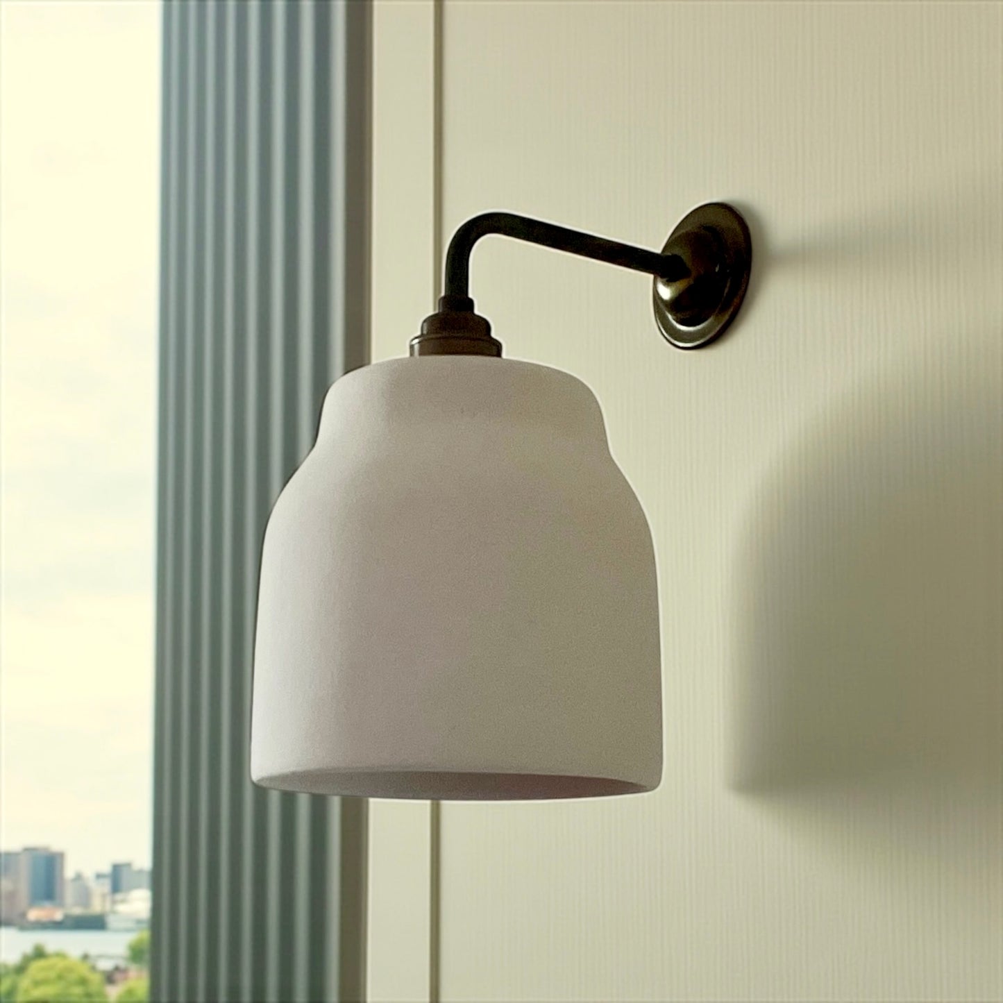 Wall-mounted lamp with white shade and brass arm against a light wall.