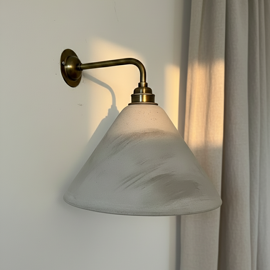 Wall-mounted lamp with a grey shade and brass arm against a light wall.