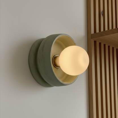 Green wall sconce with a round bulb on a neutral wall.