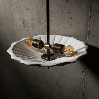 Modern pendant light with white shell-like shade and brass fixtures against a concrete wall.