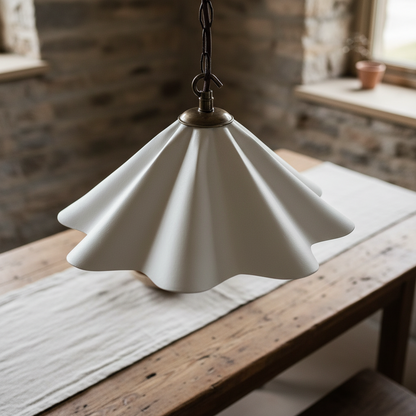 White pendant light with a scalloped design hanging over a wooden table in a rustic setting.