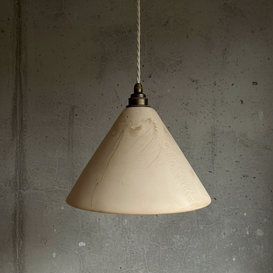 Beige cone-shaped pendant light hanging against a gray concrete wall.