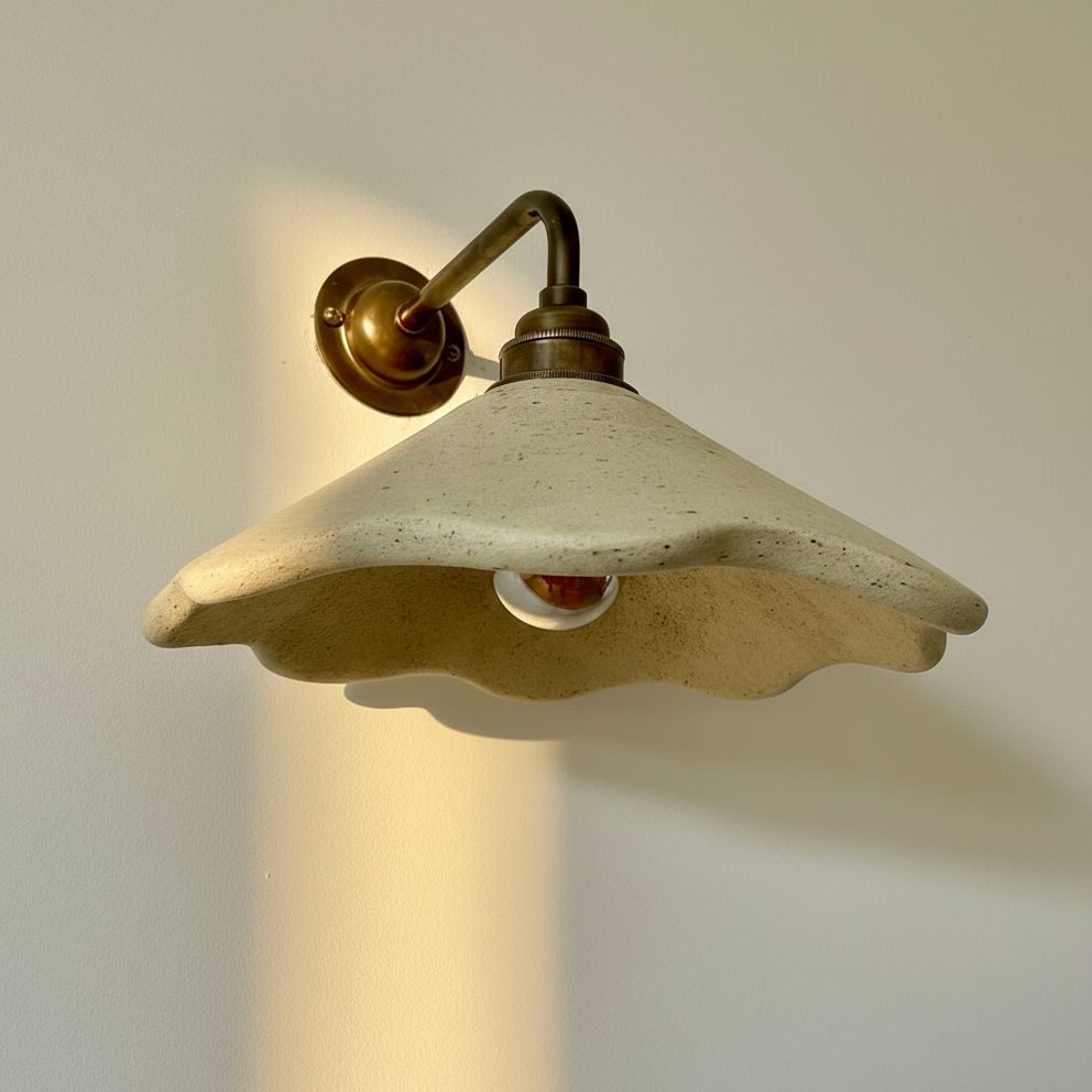 Wall light fixture with concrete shade and brass fitting on a plain wall.