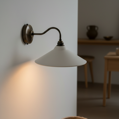 Wall-mounted lamp with a white shade casting light on a wall, with a ceramic pot on the floor.