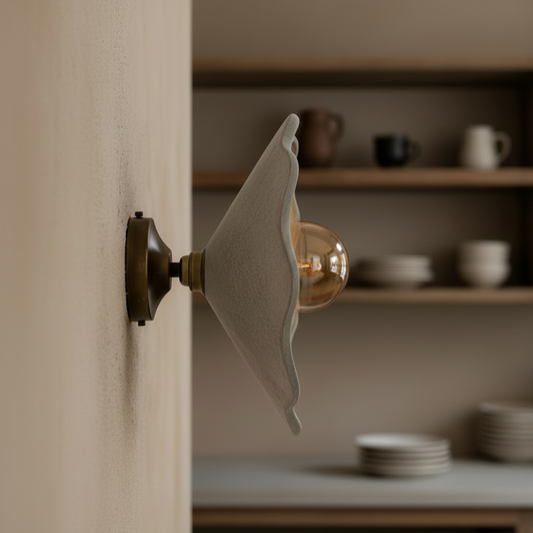 Wall-mounted light fixture with a wavy design on a neutral wall, with shelves and kitchenware in the background.