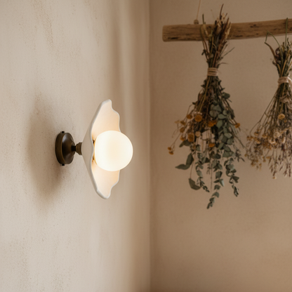 Wall-mounted light fixture with a decorative design on a neutral wall with hanging dried plants.