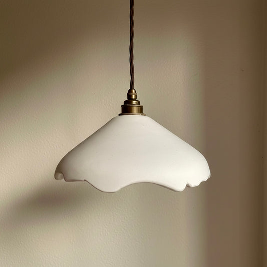 White pendant light with a scalloped edge against a beige wall